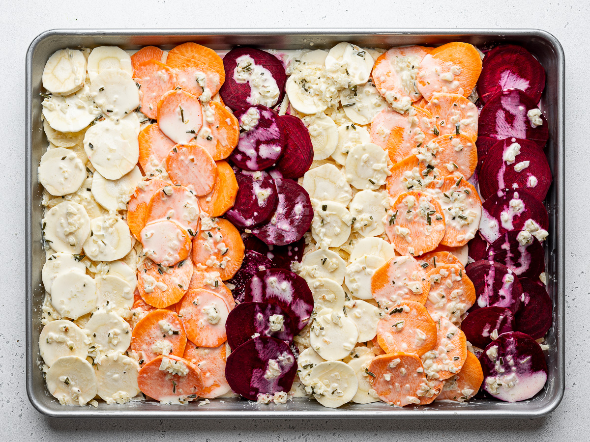 Uncooked sliced root vegetables in sheet pan prepared with cream and cheese. 