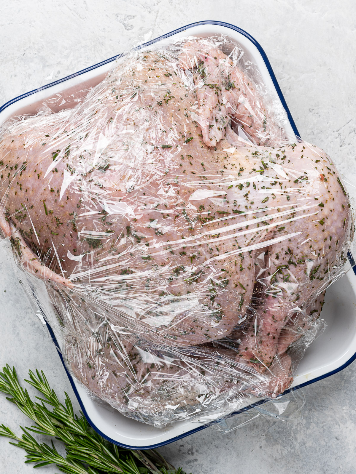 Spatchcocked turkey with dry brine wrapped with plastic in a baking pan ready for the fridge.