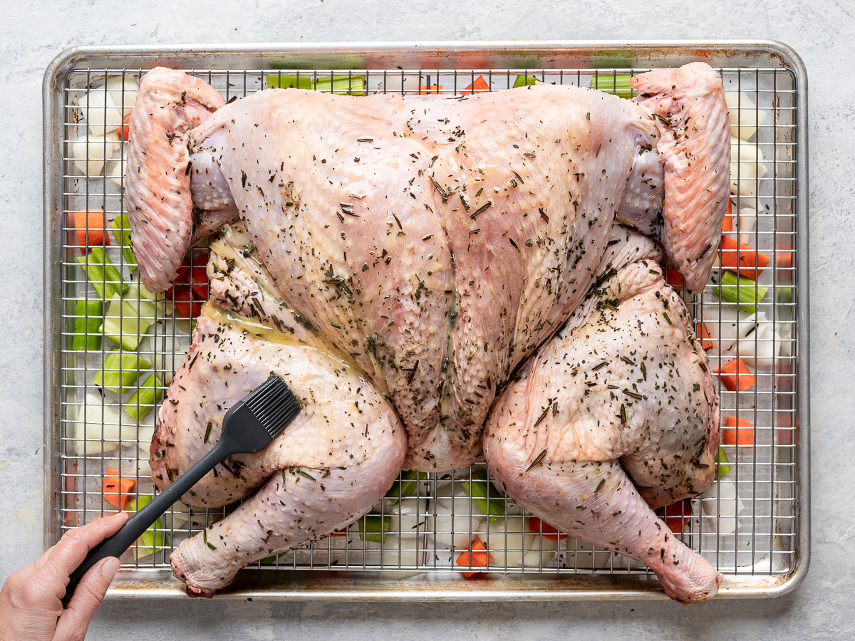 Raw spatchcocked turkey on baking sheet getting brushed with melted butter.