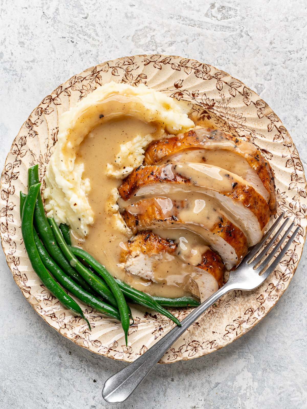 Sliced turkey and mashed potatoes served on a plate with green beans and gravy.