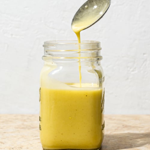 Champagne Vinaigrette in mason jar with spoon scooping out and dripping some of the vinaigrette.