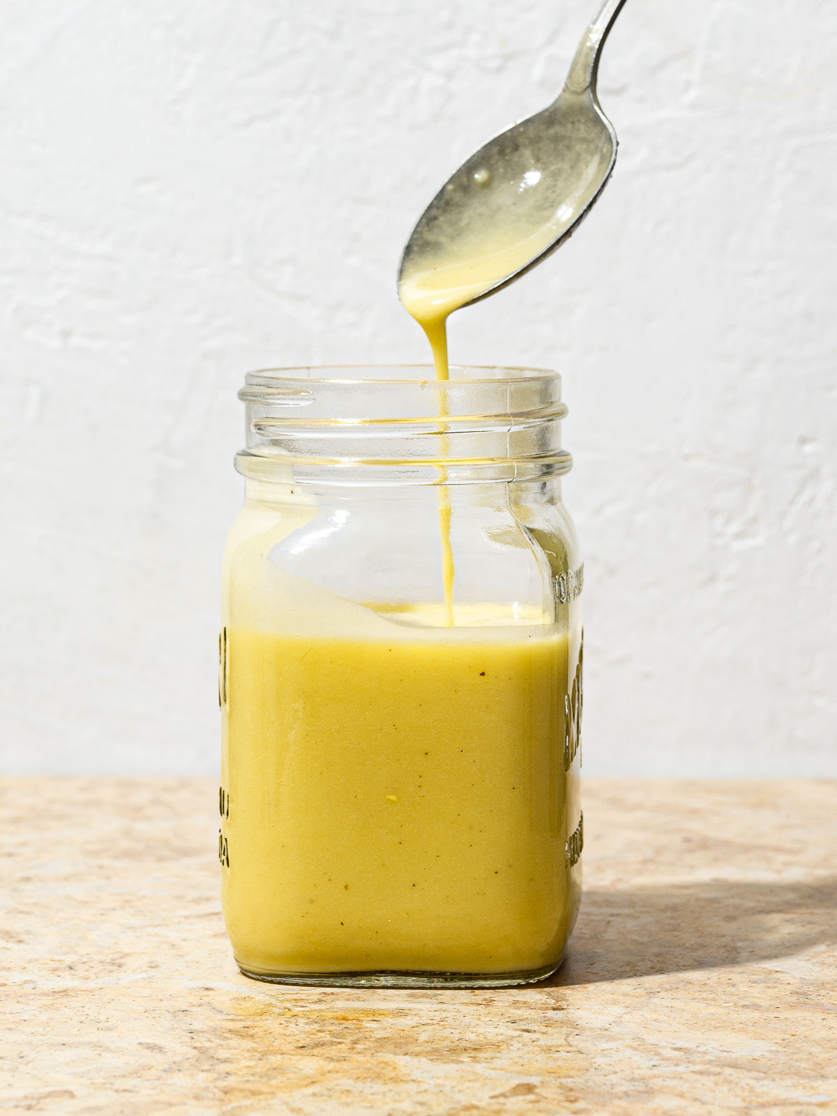 Champagne Vinaigrette in mason jar with spoon scooping out and dripping some of the vinaigrette. 