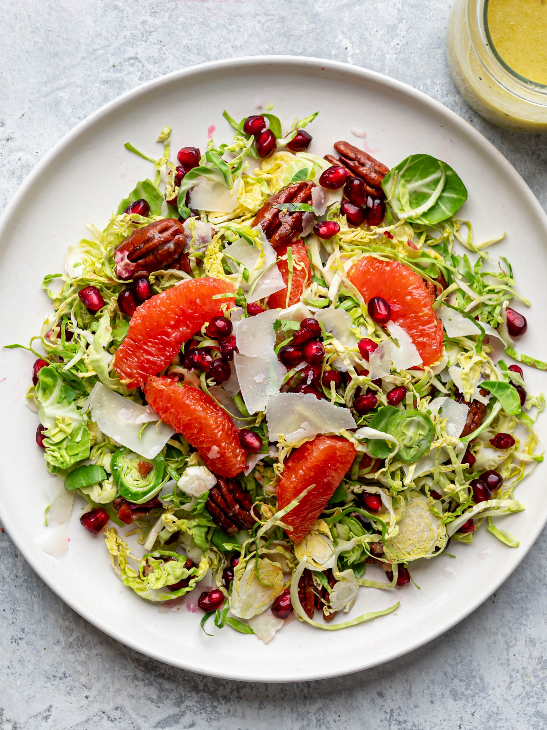 Salad with shaved Brussels sprouts, citrus, and pomegranate seeds served on white plate.