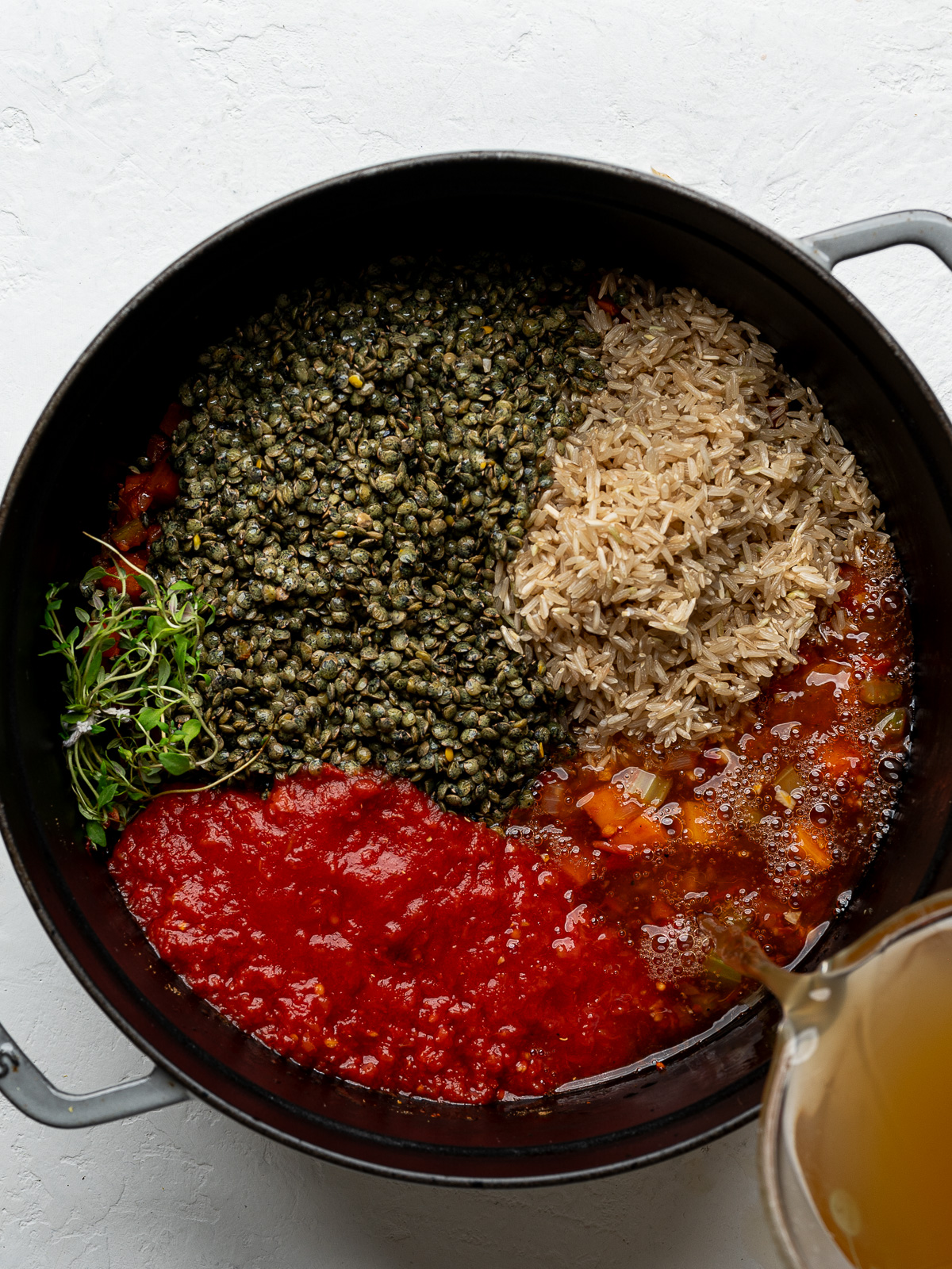 Pouring broth over lentils and rice in Dutch oven.