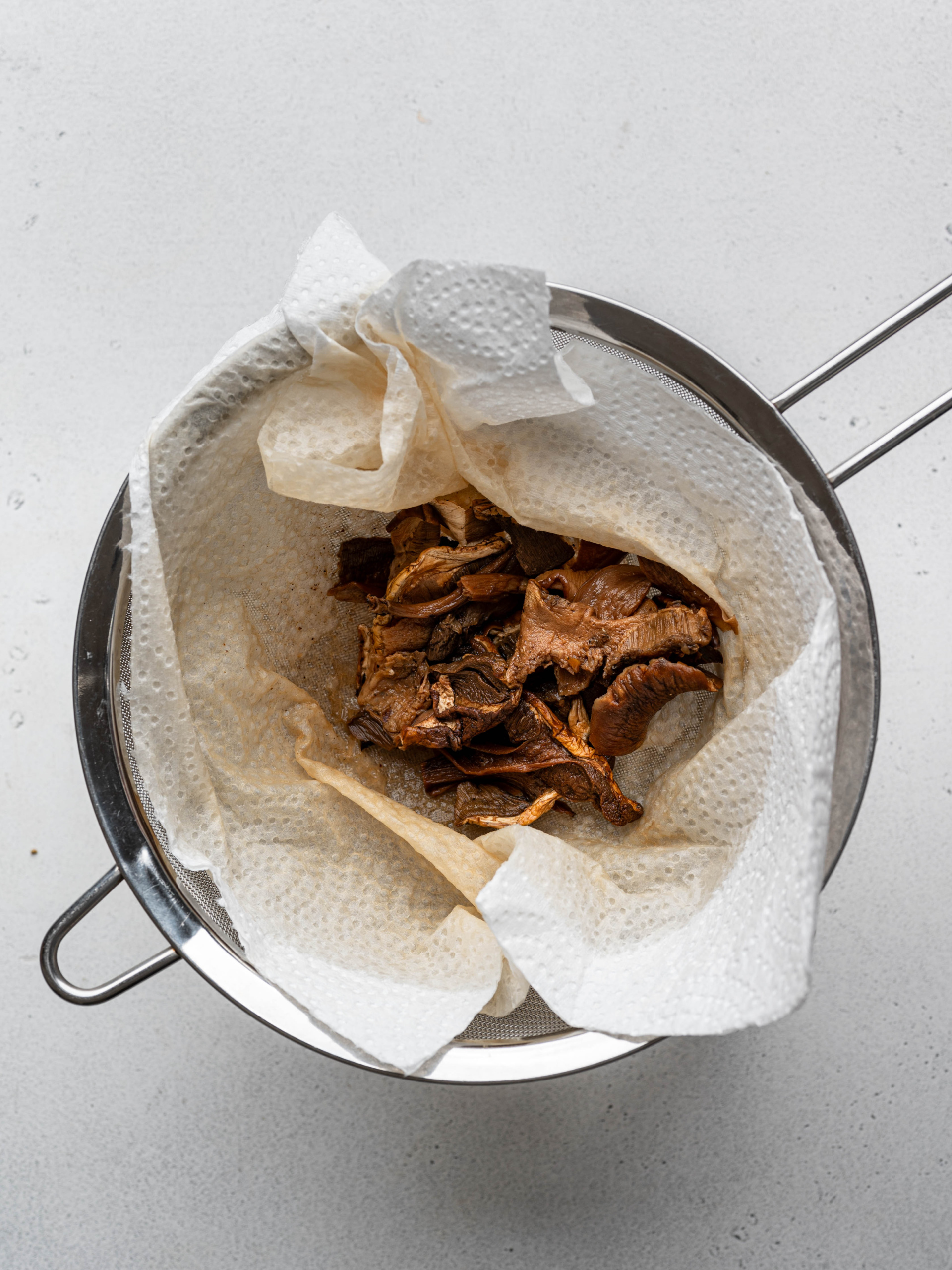 Dried porcini mushrooms strained over sieve. 