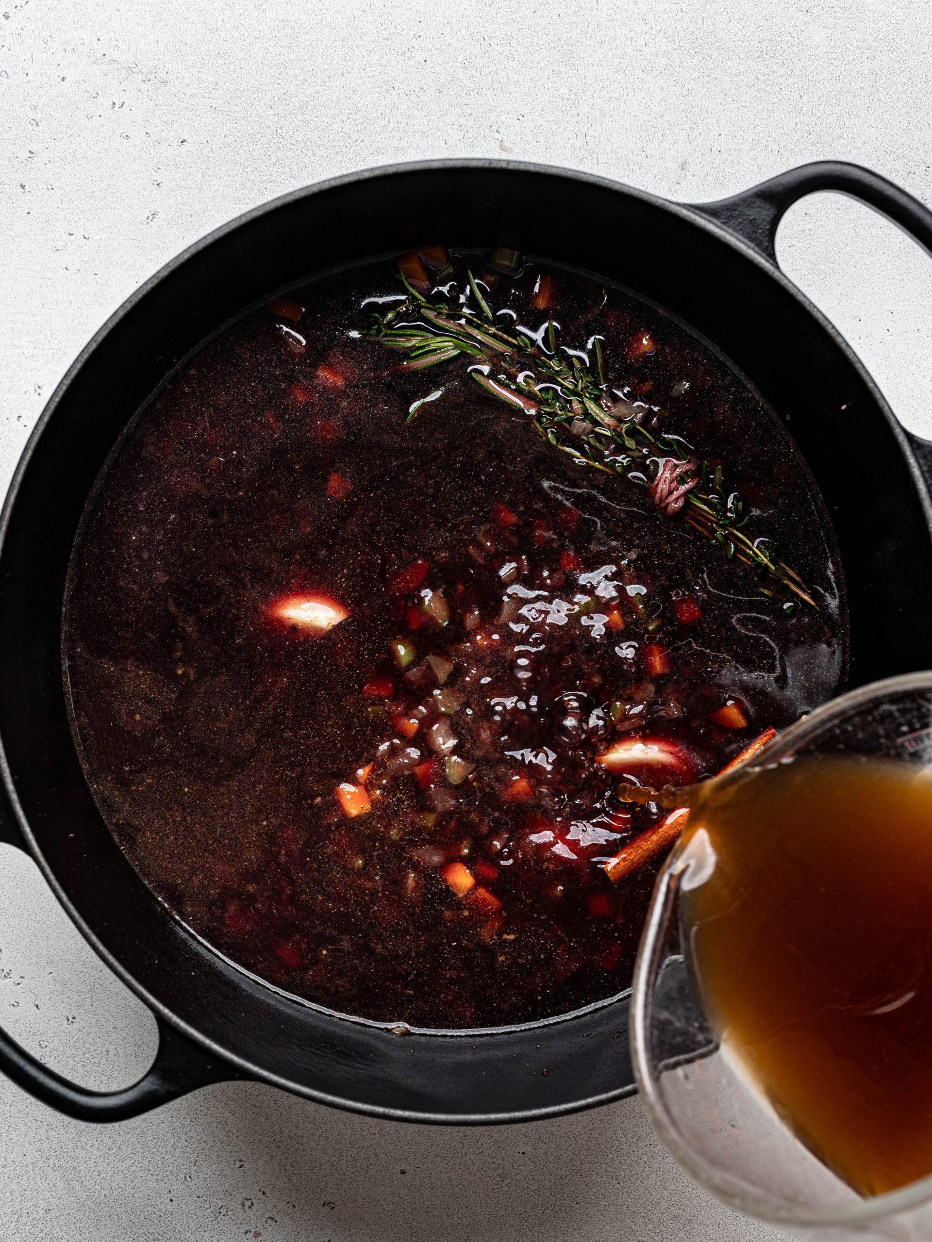 Pouring broth into pot over wine mixture. 