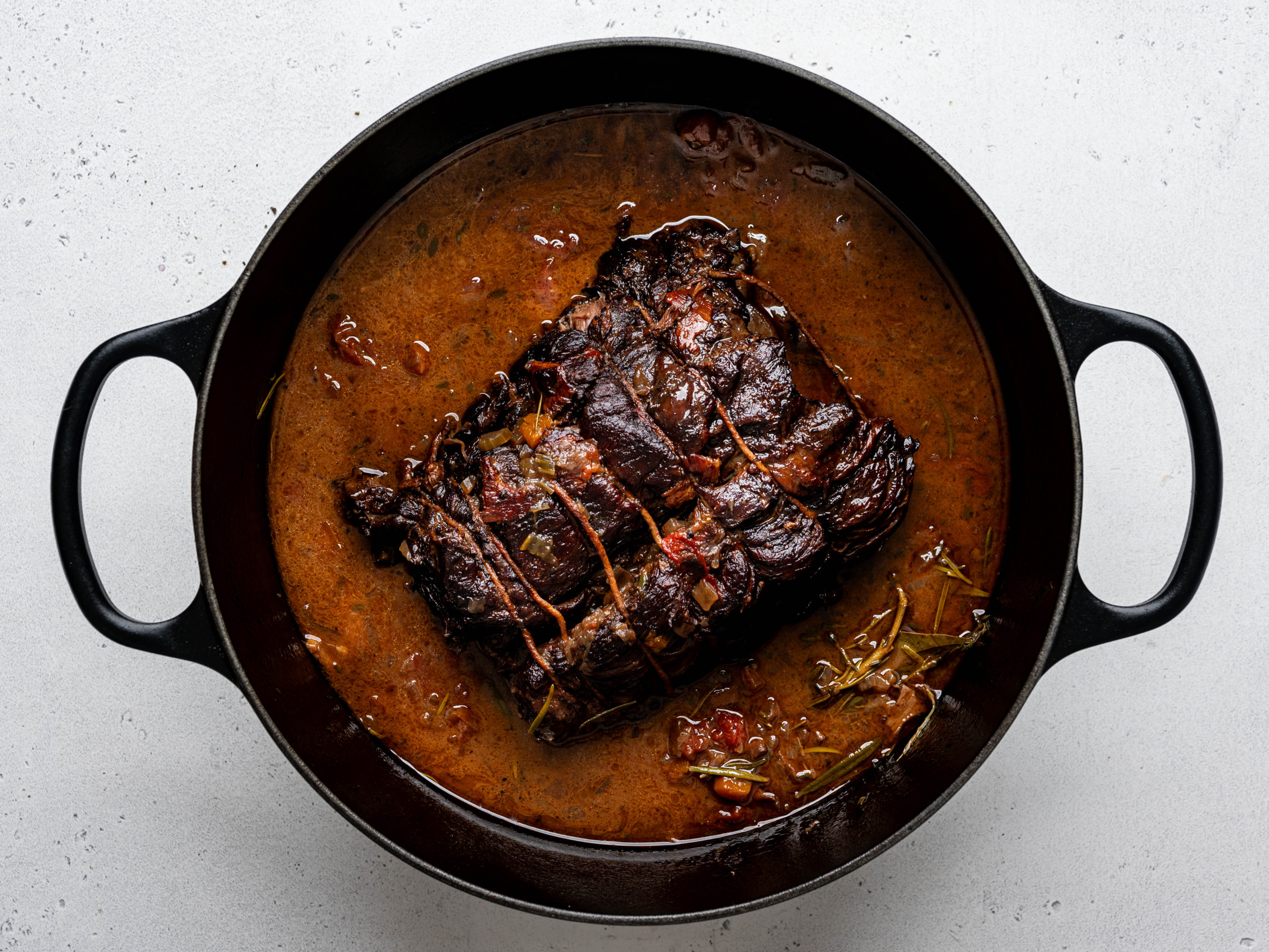 Braised Stracatto di manzo (Italian pot roast) sitting in the braising liquids in a large black Dutch oven. 