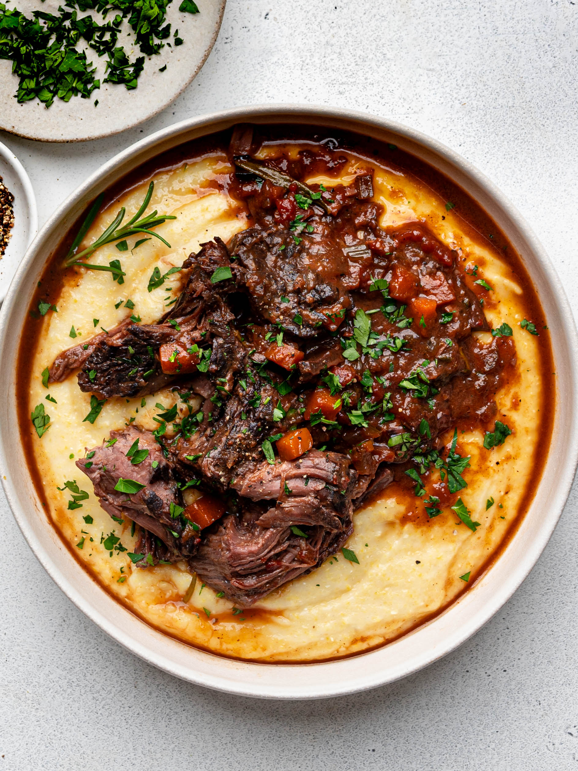 Yellow polenta in a shallow bowl topped with shredded chunks of Stracatto di manzo (Italian pot roast) and sauce. 