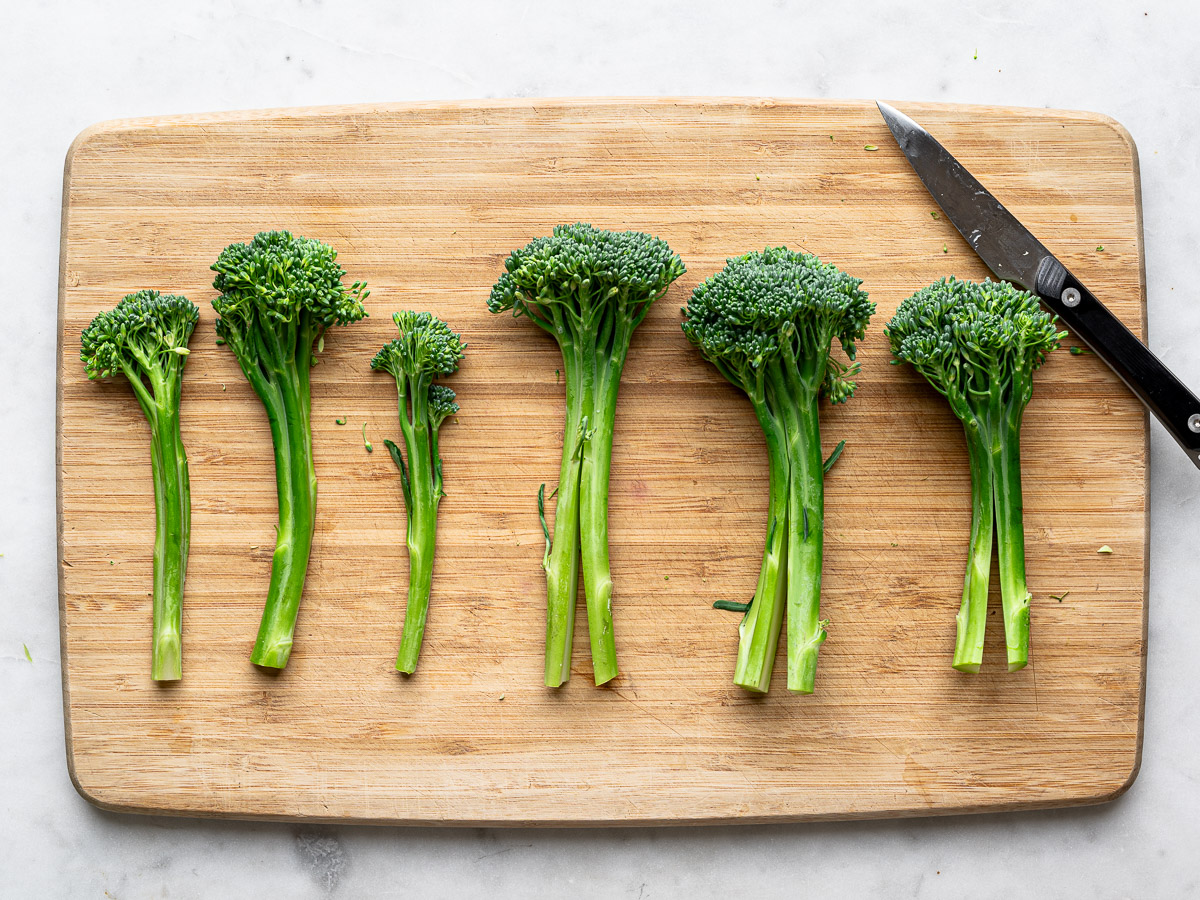 Broccolini stalks getting trimmed on cutting board. 