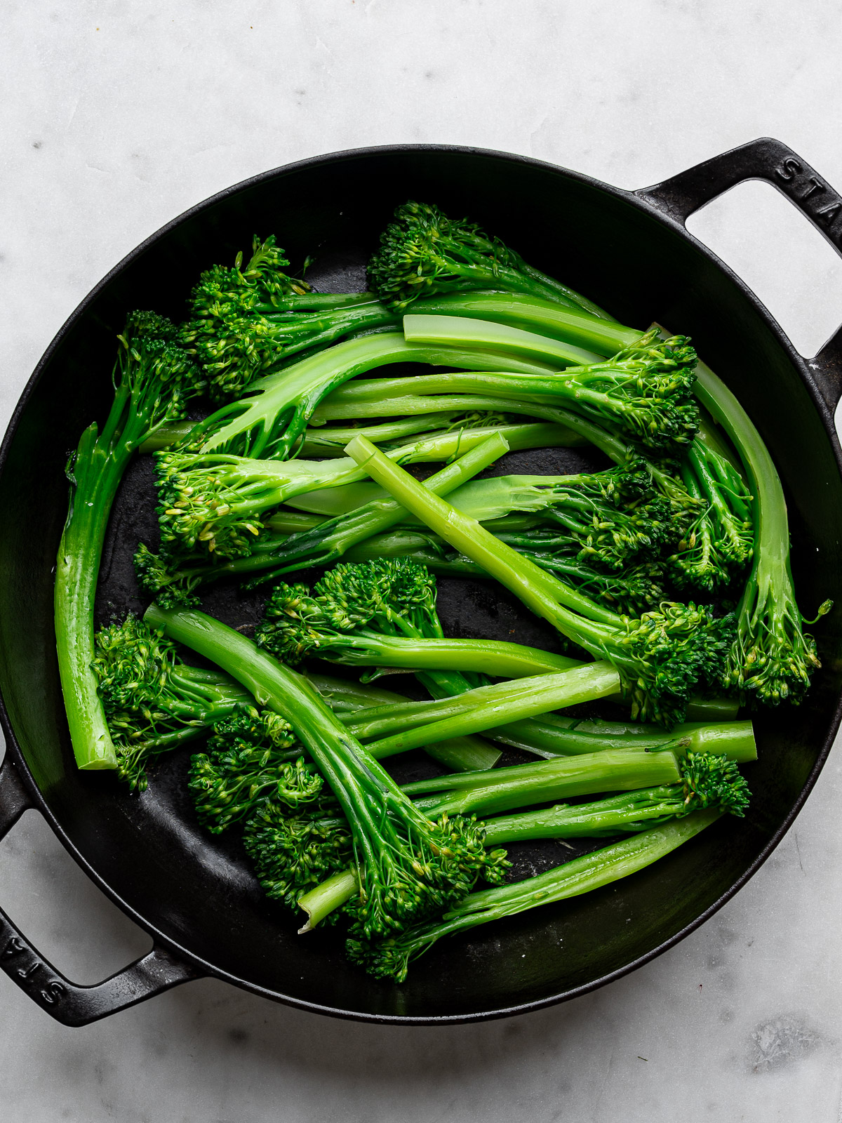 Steamed broccolini stalks in black skillet. 