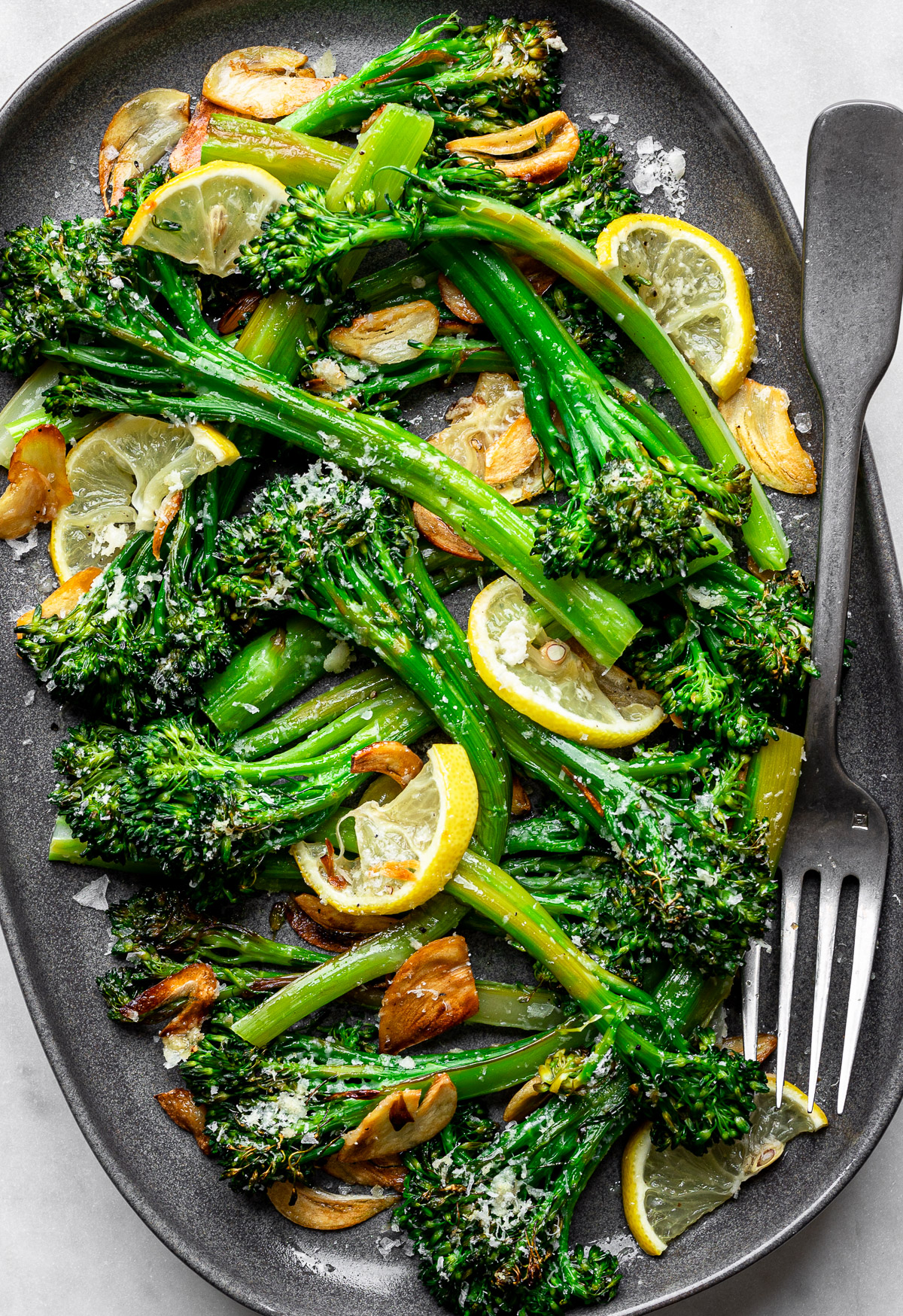 Lemon Parmesan Broccolini served on a tray oval platter topped with crispy garlic chips.