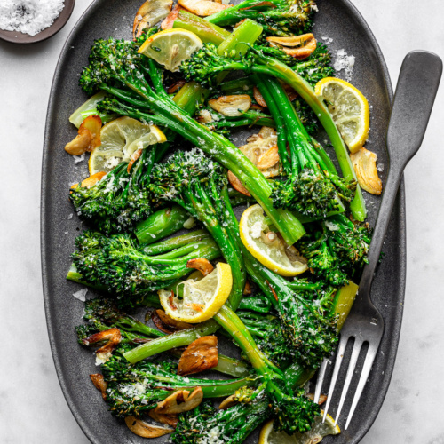 Lemon Parmesan Broccolini served on a tray oval platter topped with crispy garlic chips.
