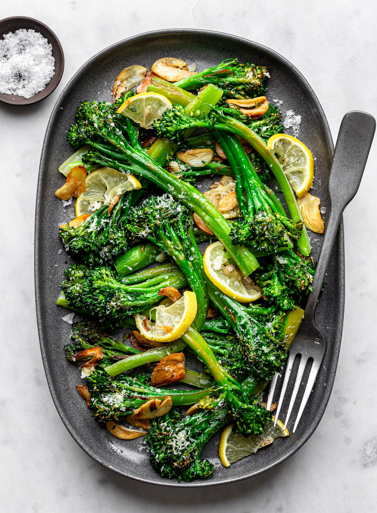 Lemon Parmesan Broccolini served on a tray oval platter topped with crispy garlic chips. 