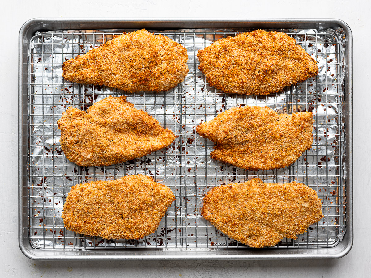 Six baked crispy chicken cutlets on a wire rack set over a sheet pan.