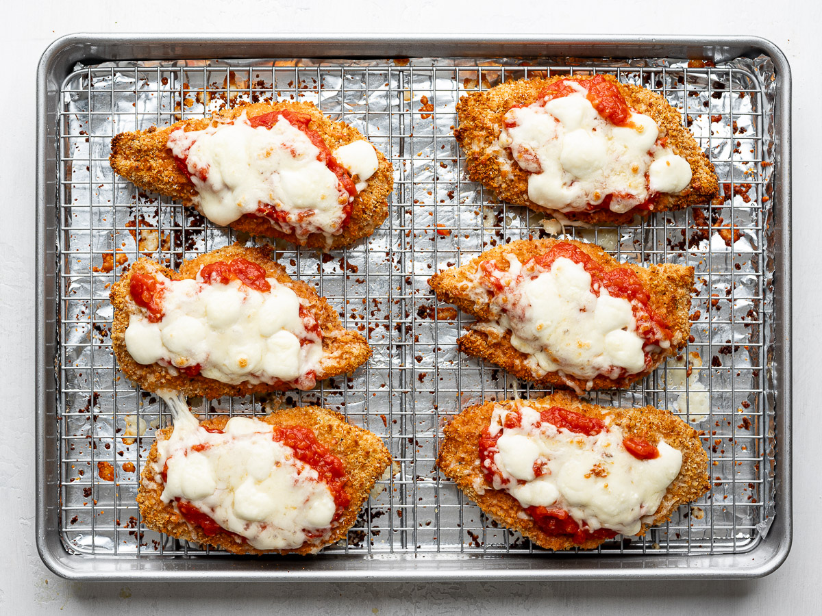Six chicken parmesan pieces on a sheet pan with sauce melty cheese from the broiler. 