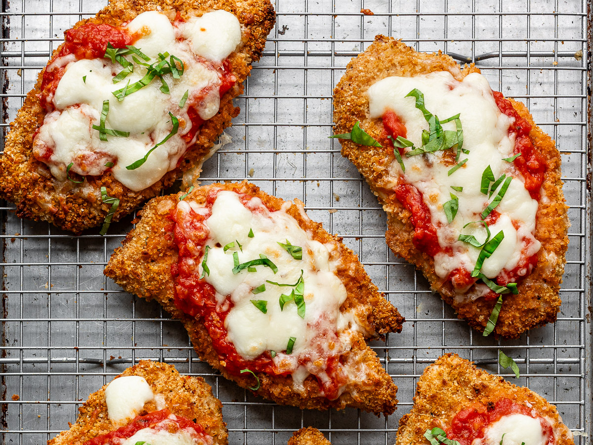 Close-up of baked chicken parmesan cutlets on a wire rack garnished with fresh basil. 