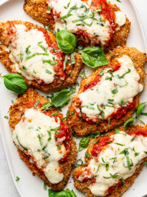 Baked Parmesan chicken pieces served on a white platter with fresh basil leaves.