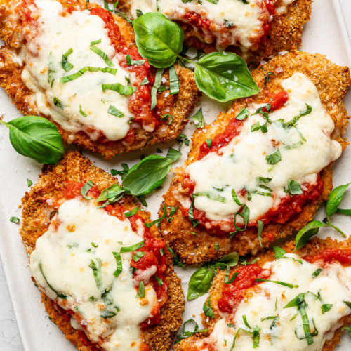 Baked Parmesan chicken pieces served on a white platter with fresh basil leaves.