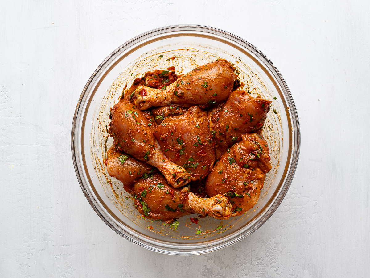 Chicken pieces marinating in glass mixing bowl.