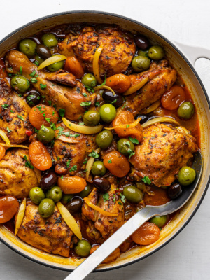Close up of prepared chicken tagine with olives and apricots in a white braiser.
