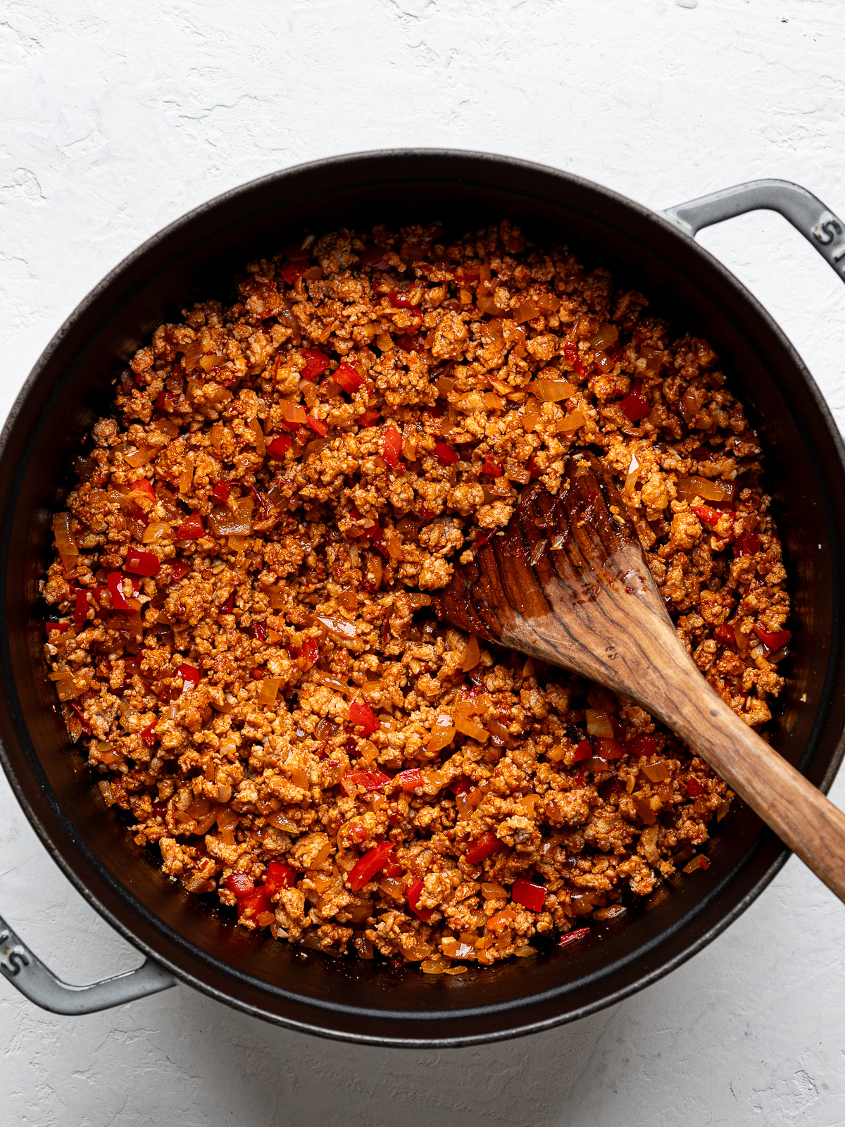 Cooked ground turkey and veggie mixture with harissa and tomato paste in gray Dutch oven.