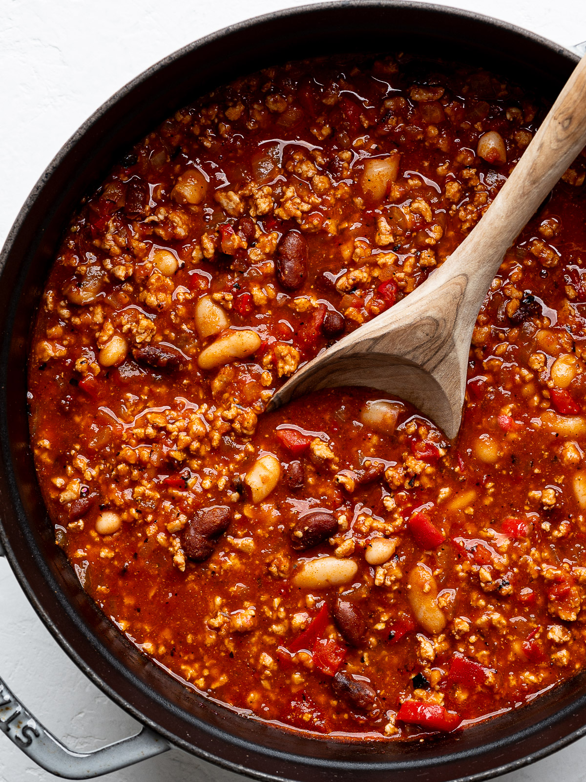 Close up of cooked chili in Dutch oven with wooden spoon.