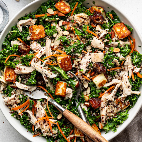 Assembled Kale and quinoa salad with shredded chicken and halloumi in a large white salad bowl.