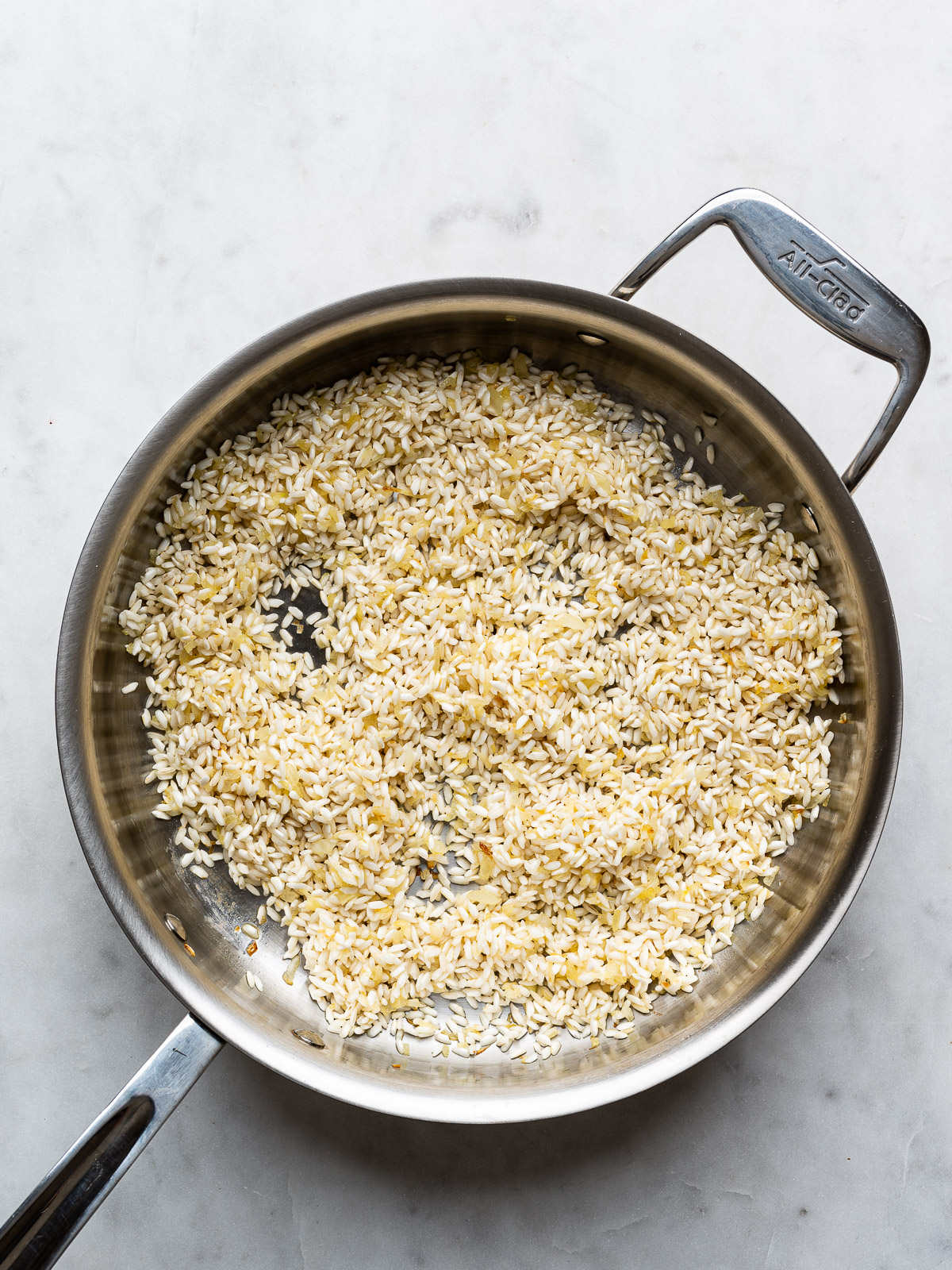 Rice grains toasted with onions in stainless steel skillet.