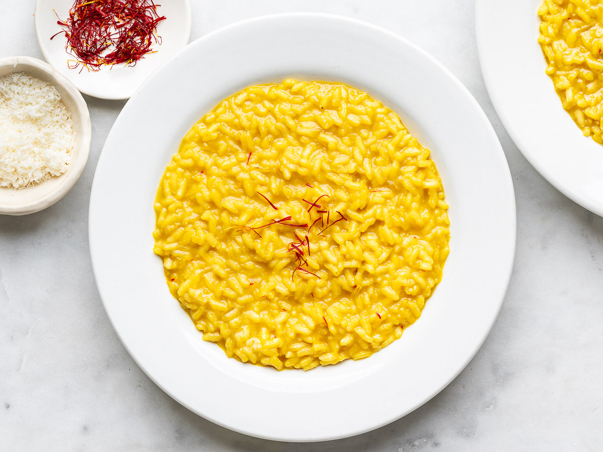Risotto Milanese served in two white bowls with small bowl of saffron threads on the side. 