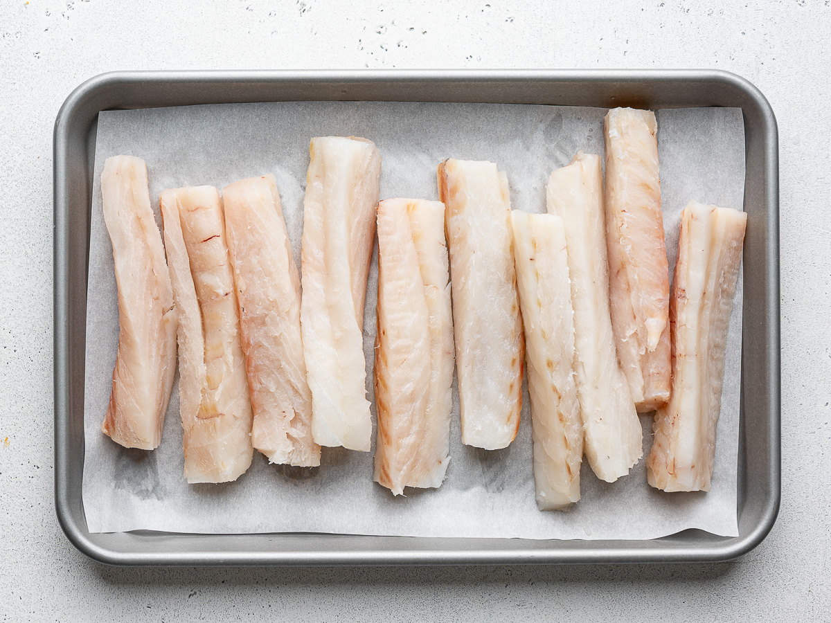 1x4-inch pieces of raw cod fish on a parchment-lined baking sheet. 