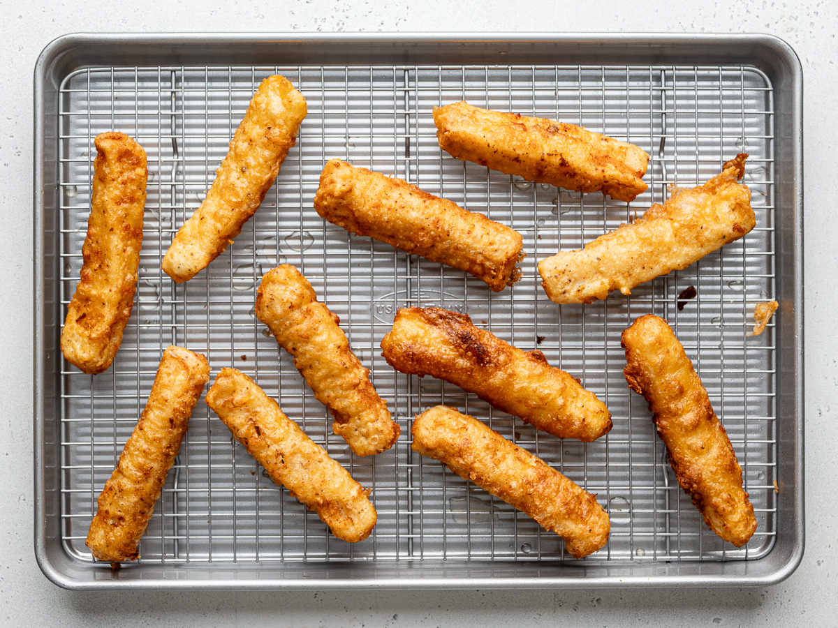 All of the fried fish pieces draining on a wire rack. 