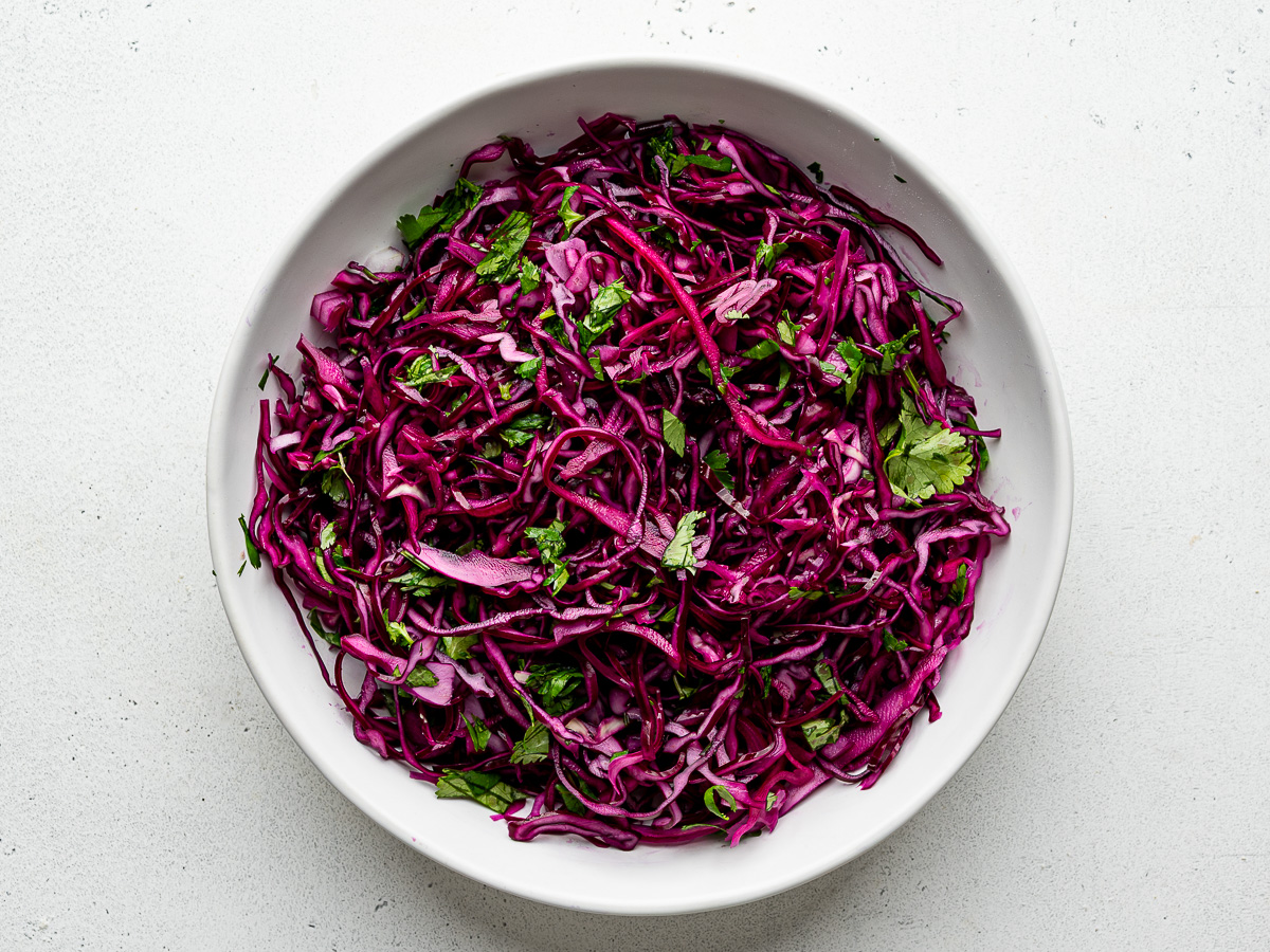 Red cabbage slaw prepared in a white bowl.