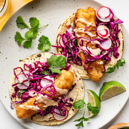 Two assembled Baja fish tacos with coleslaw on a light coloured plate.