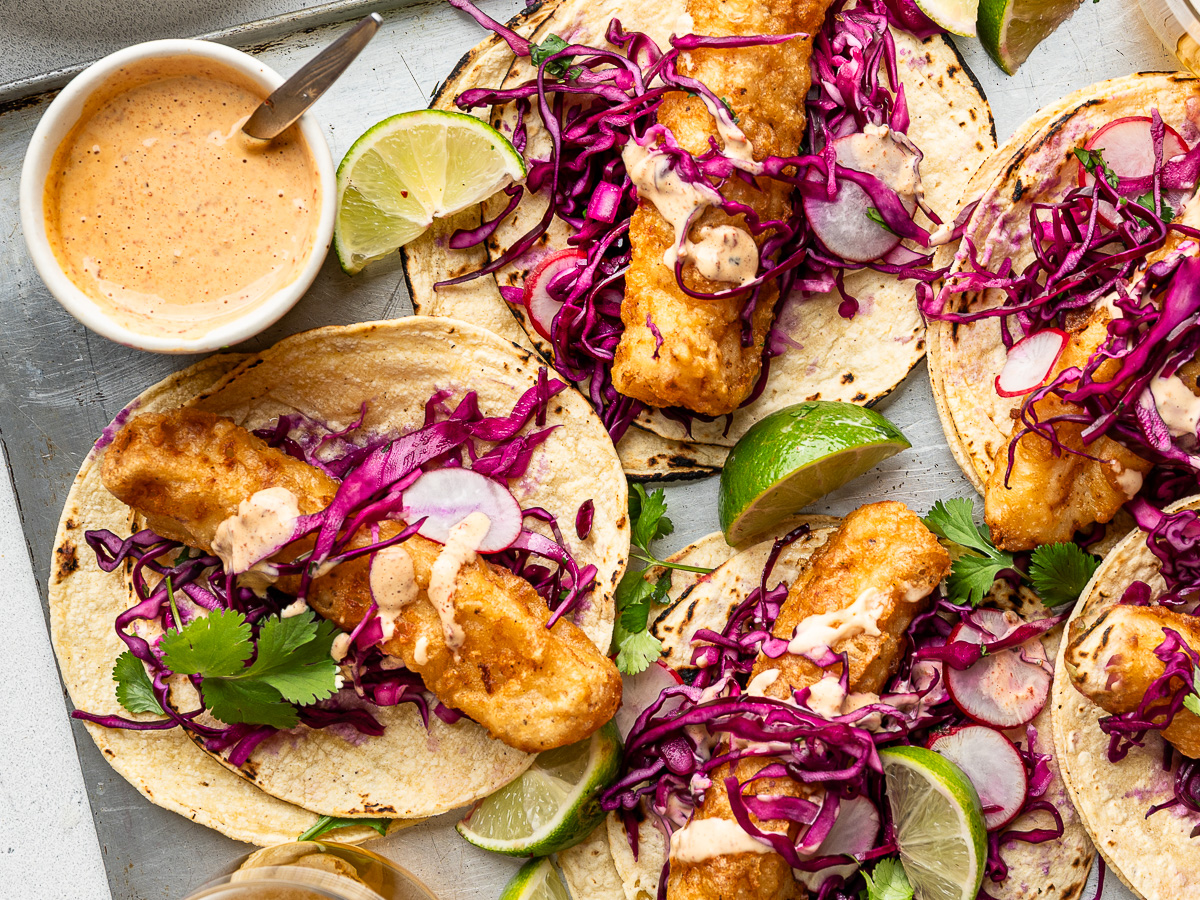 Close-up of assembled baja fish tacos with chipotle sauce on the side.
