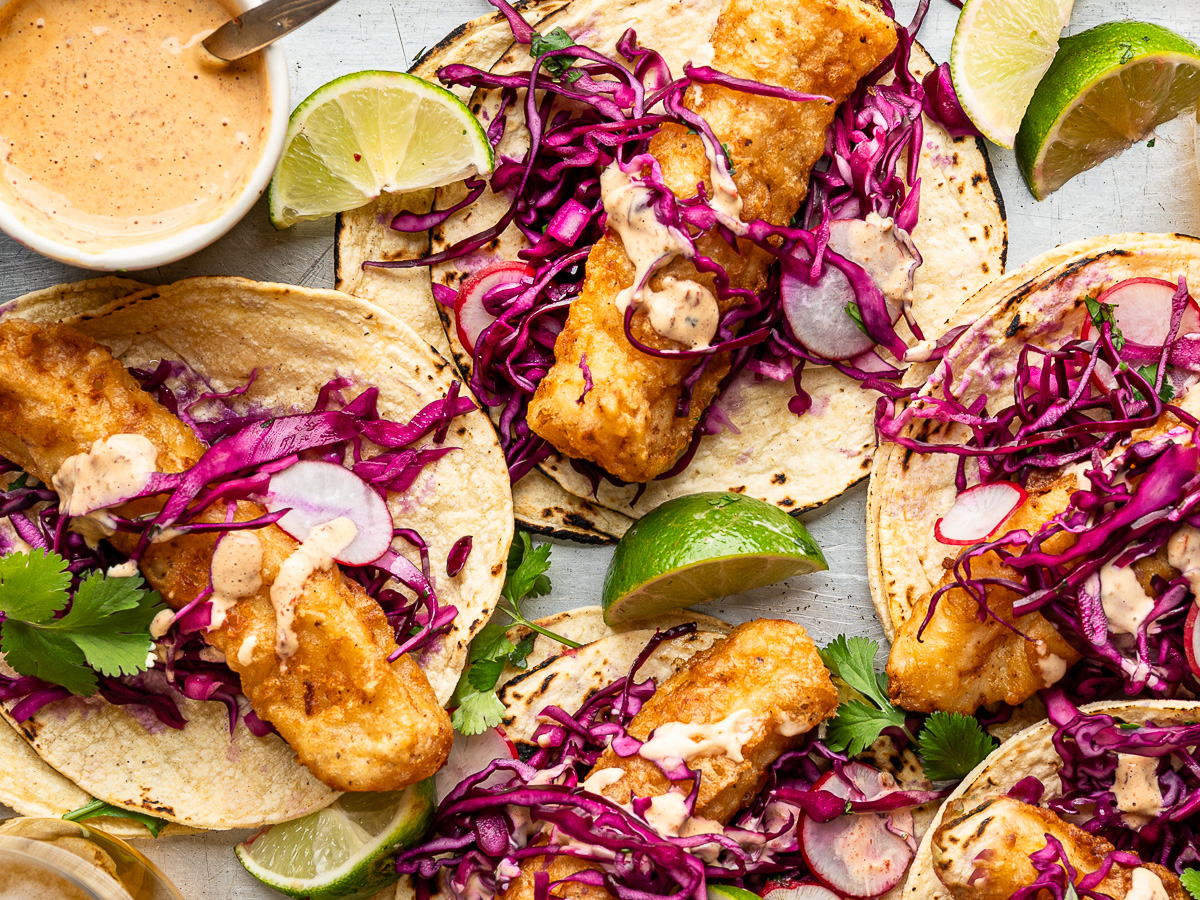 Close-up of assembled baja fish tacos with chipotle sauce on the side.