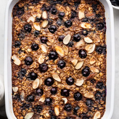 Close up of Blueberry Baked Oatmeal topped with sliced toasted almonds in white rectangular baking dish.