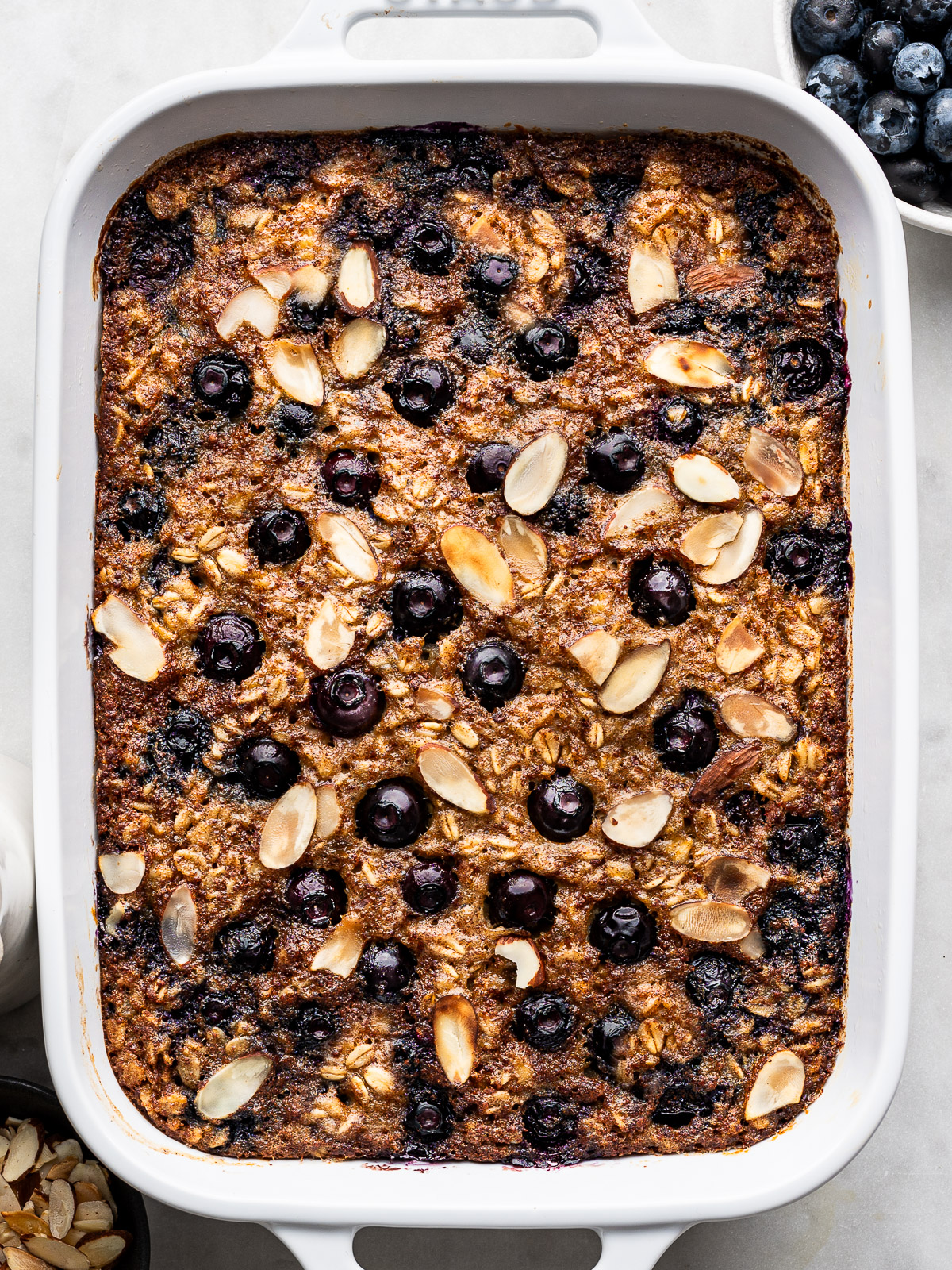 Close up of Blueberry Baked Oatmeal topped with sliced toasted almonds in white rectangular baking dish.