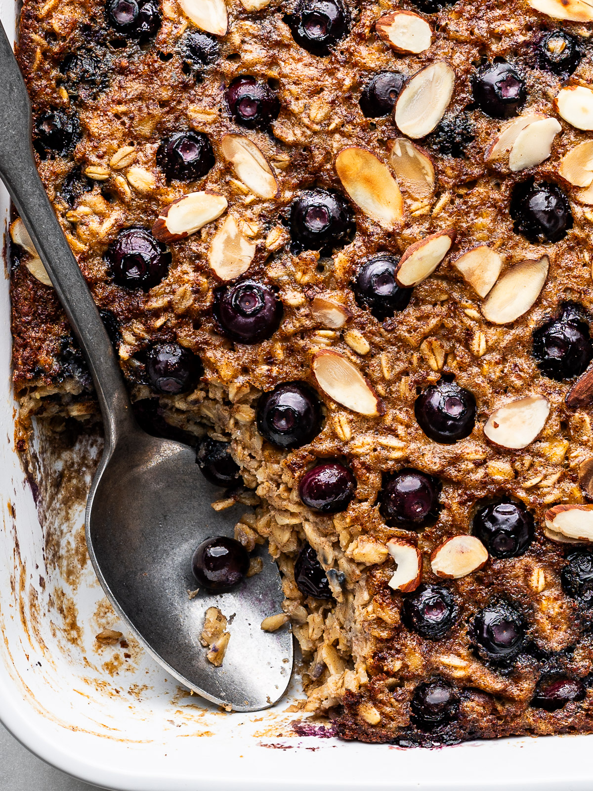 Close up of spoon scooping out baked oatmeal from baking dish.