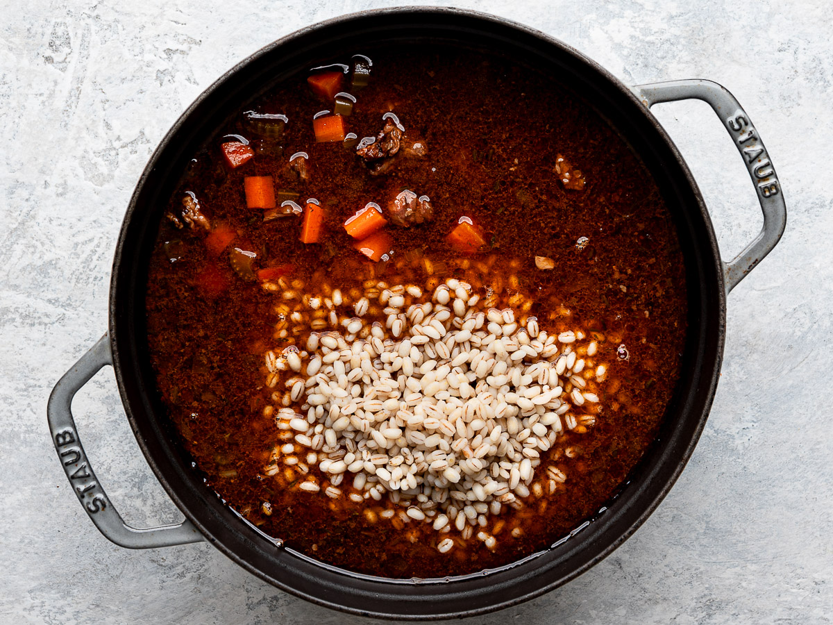 Adding pre-cooked barley to stewed meat in pot. 