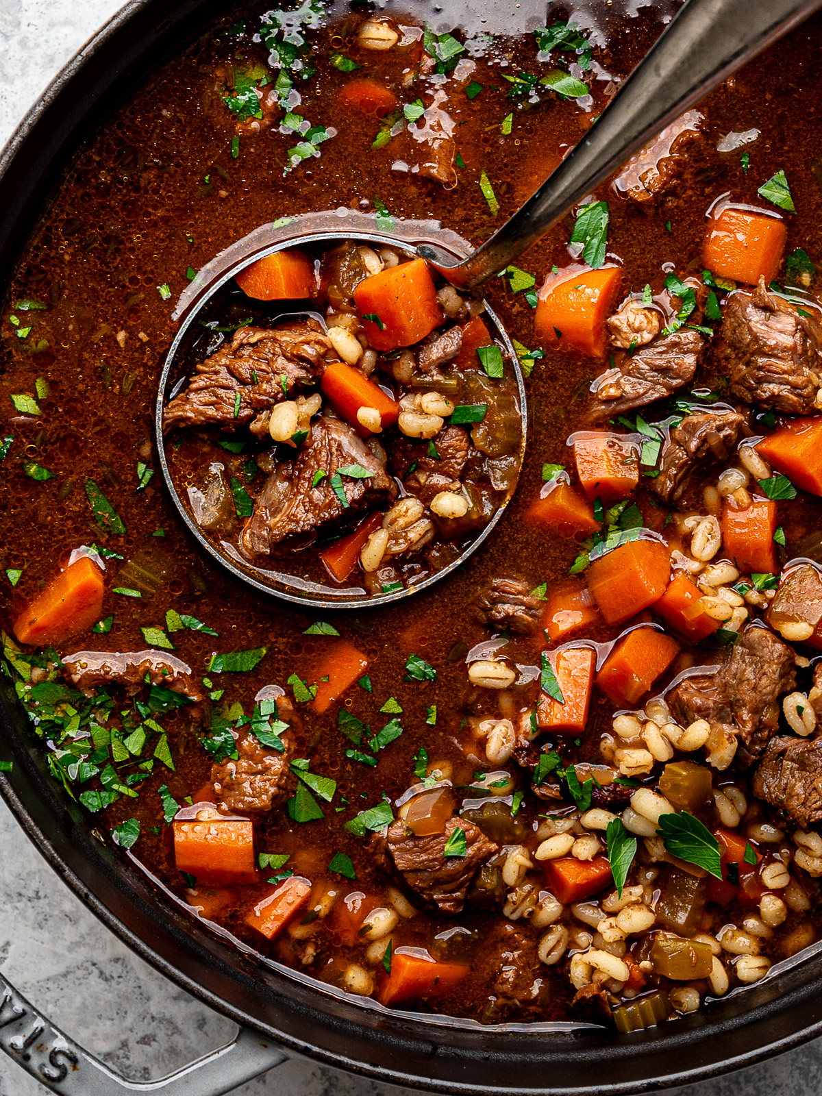 Close-up of ladle scooping out cooked beef and barley soup.