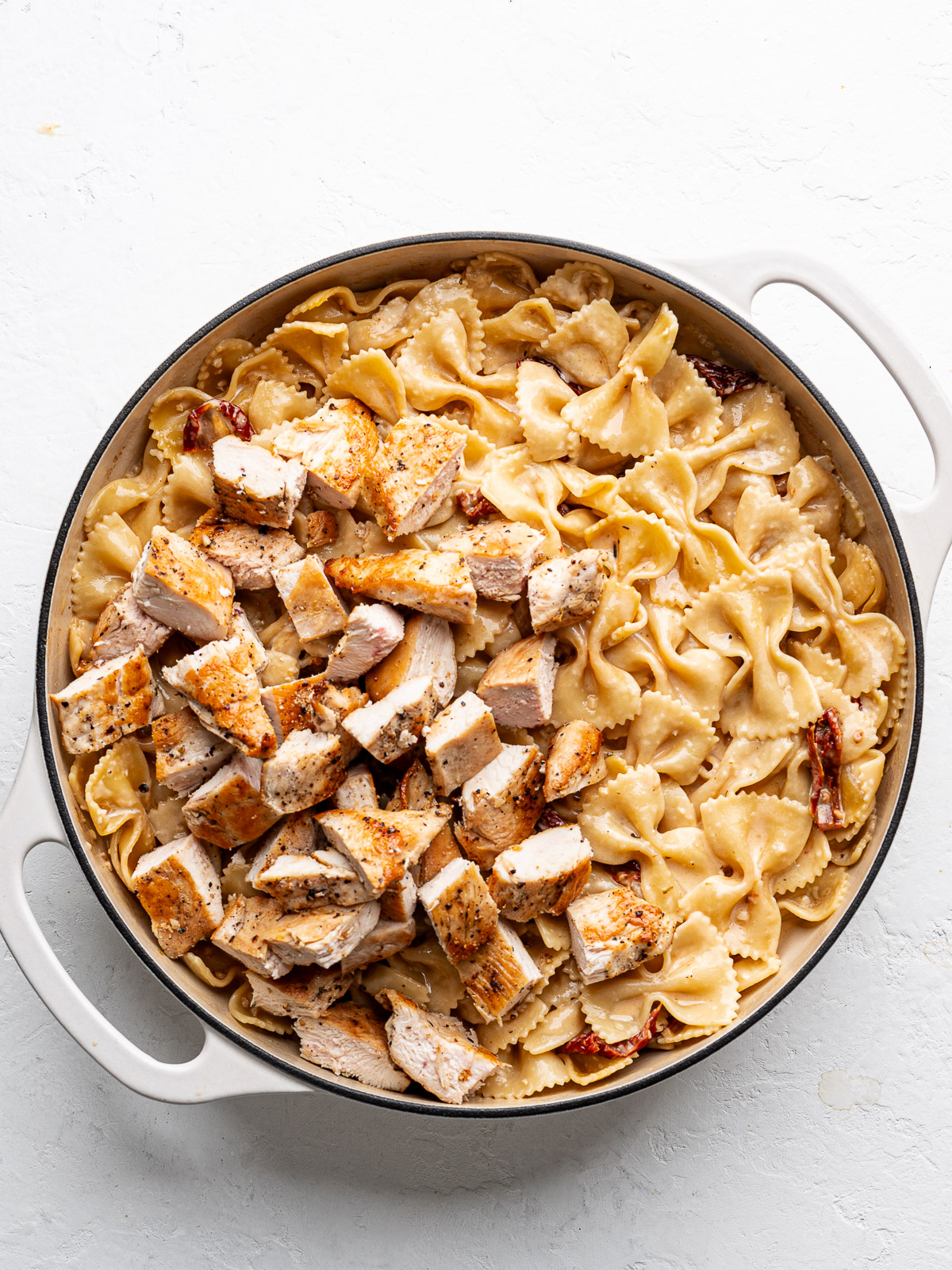 Cooked chicken pieces added to cooked pasta in skillet. 