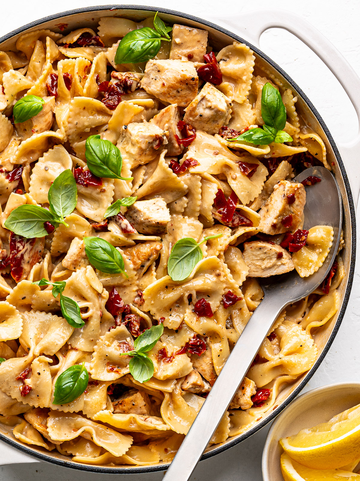 Close-up of the finished dish of marry me chicken pasta in a large white skillet with a serving spoon.