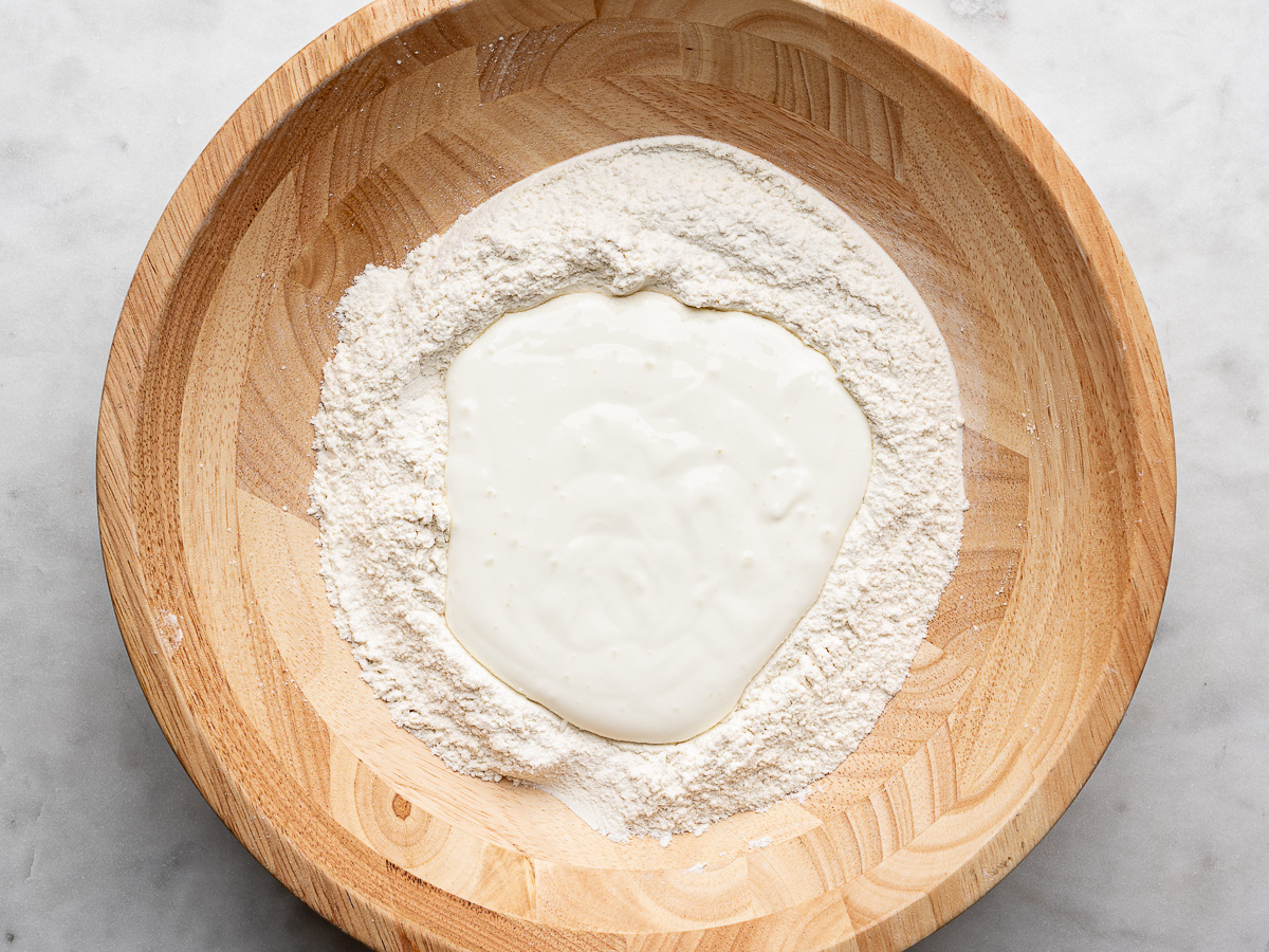 Flour mixture in a wooden bowl with whipped cottage cheese in the middle. 