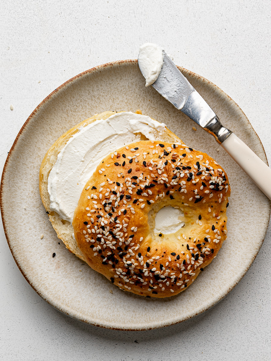 One sliced cottage cheese bagel on a small plate slathered with cream cheese. 