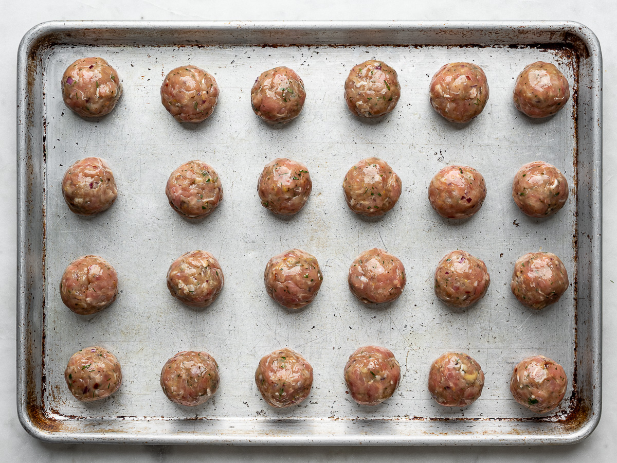Rolled, uncooked meatballs on baking sheet. 
