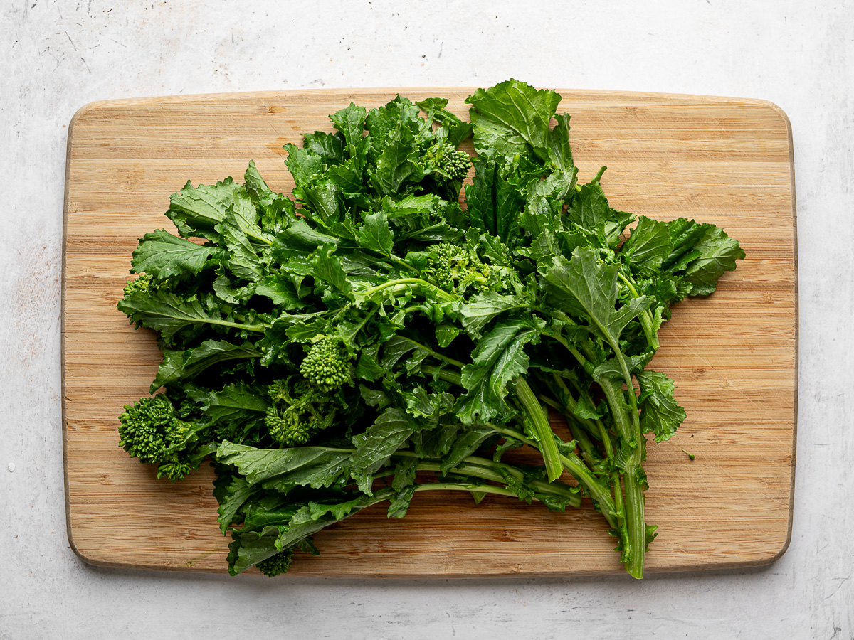 A large bunch of rapini (broccoli rabe) on a wood cutting board. 