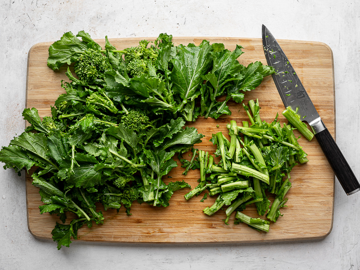 A large bunch of chopped rapini (broccoli rabe) on a wood cutting board with a chef's knife. . 