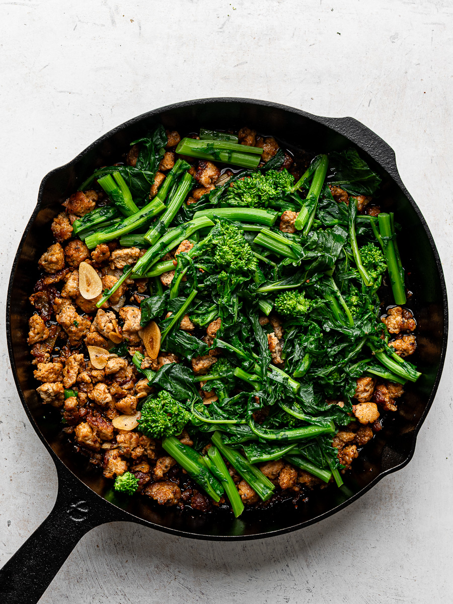 Blanched rapini added to sausage mixture in skillet. 