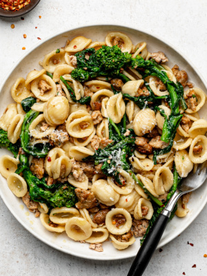 Rapini with sausage and orecchiette served on a white plate with a fork.