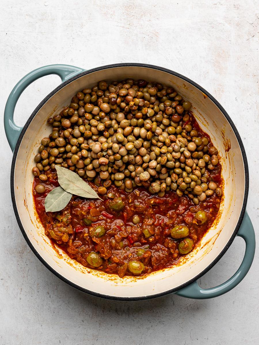 Pigeon peas added to sautéed aromatics and tomato sauce in pot. 